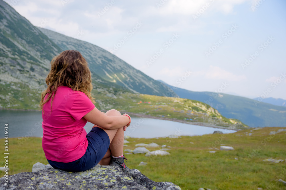 Girl sitting on a big rock over Bucura Lake, Retezat National Park, Romania Girl sitting on a big rock over Bucura Lake, Retezat National Park, Romania