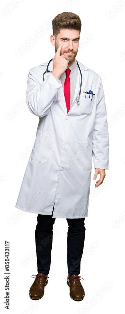 Young handsome doctor man wearing medical coat Pointing to the eye watching you gesture, suspicious expression Young handsome doctor man wearing medical coat Pointing to the eye watching you gesture, suspicious expression