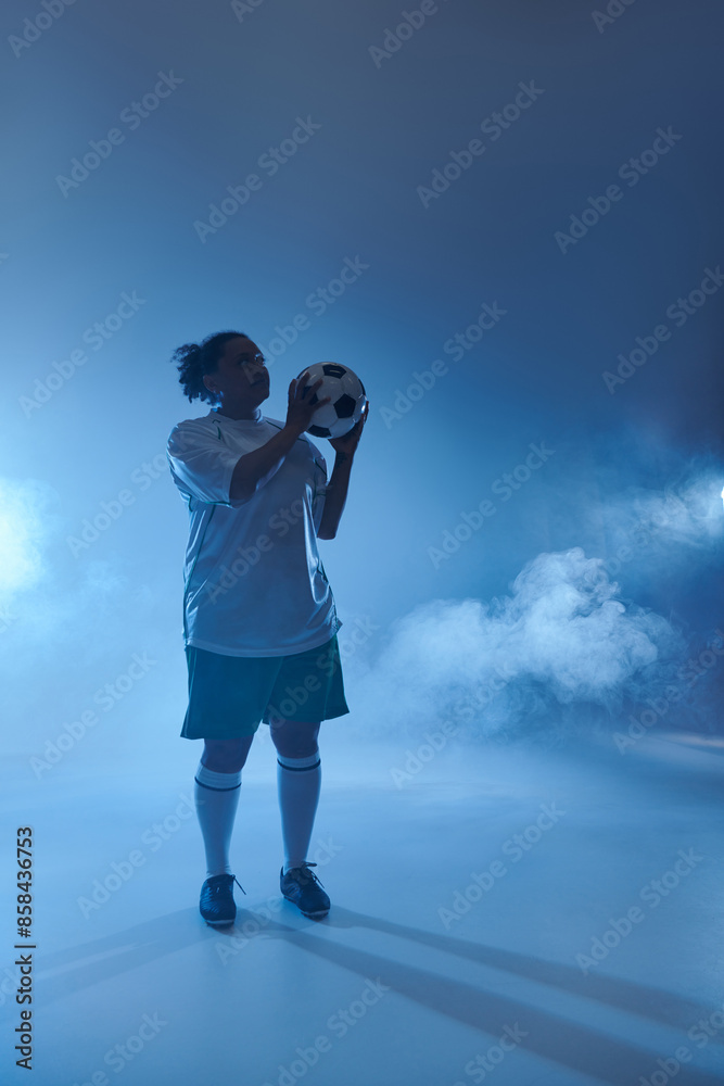 A female soccer player stands ready to play, holding the ball in her hands with determination. A female soccer player stands ready to play, holding the ball in her hands with determination.