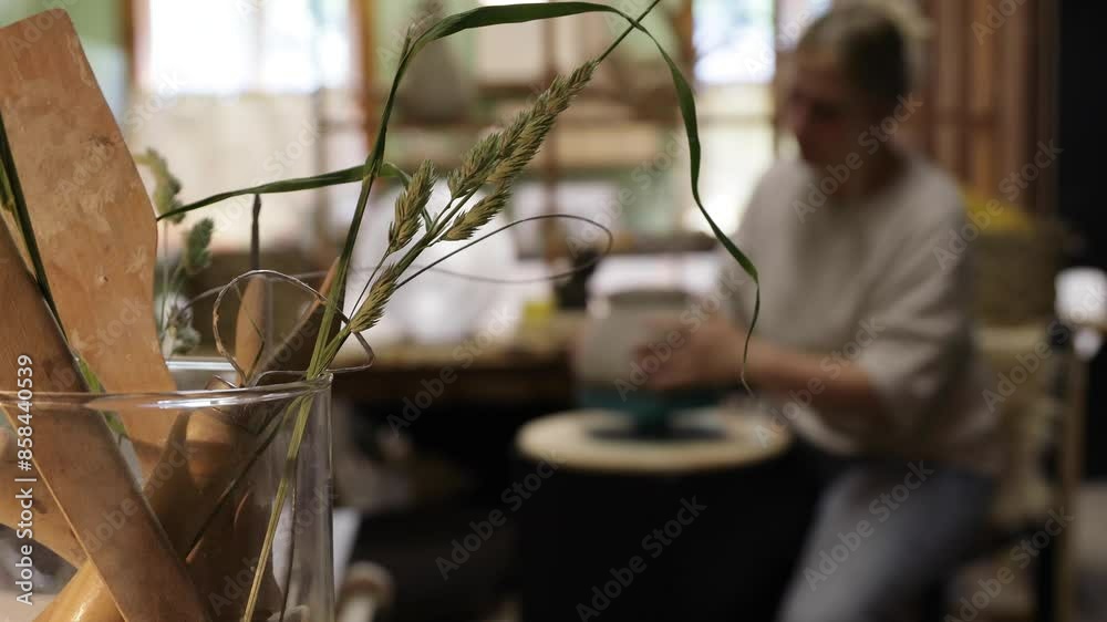 blurred background, a woman potter in her studio molding a vase on a potter's wheel