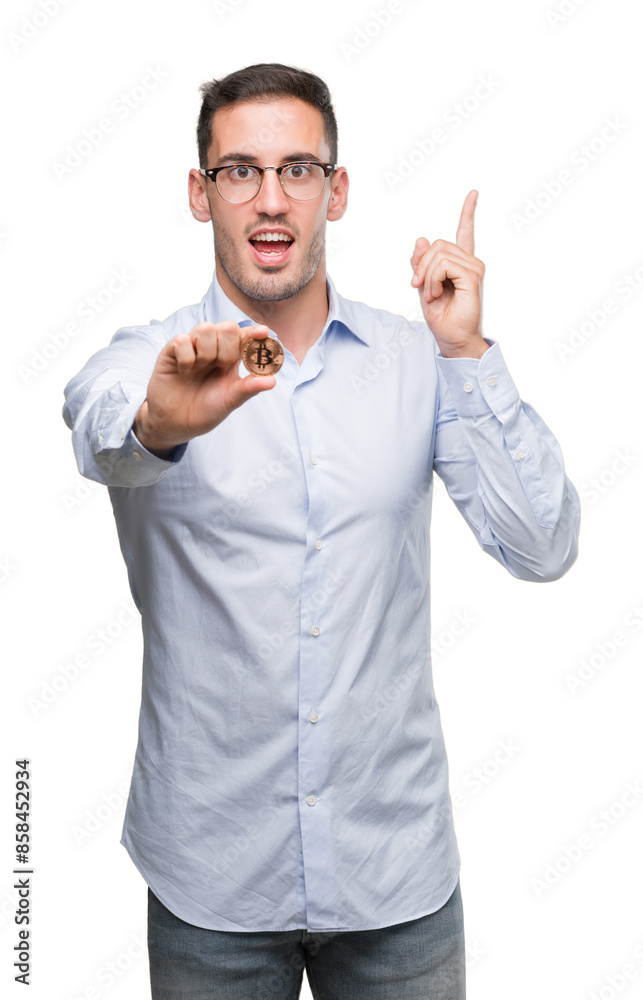 Handsome young man holding bitcoin surprised with an idea or question pointing finger with happy face, number one Handsome young man holding bitcoin surprised with an idea or question pointing finger with happy face, number one