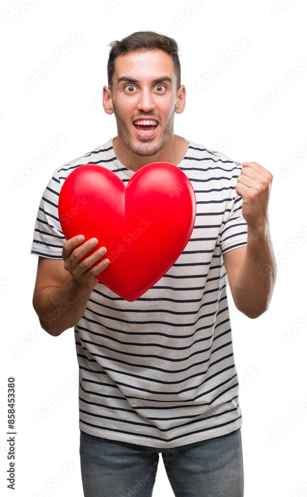 Handsome young man in love holding red heart screaming proud and celebrating victory and success very excited, cheering emotion Handsome young man in love holding red heart screaming proud and celebrating victory and success very excited, cheering emotion