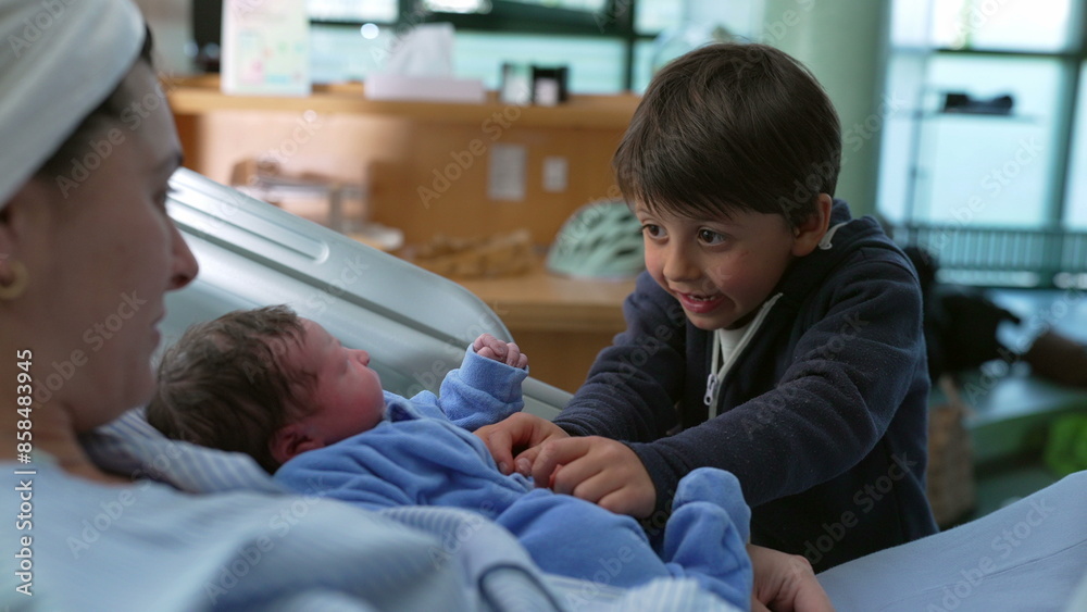 Bonding family moment of sibling interacting with his newborn baby brother at hospital after childbirth while mother watches laid in bed, young boy tickling infant Bonding family moment of sibling interacting with his newborn baby brother at hospital after childbirth while mother watches laid in bed, young boy tickling infant
