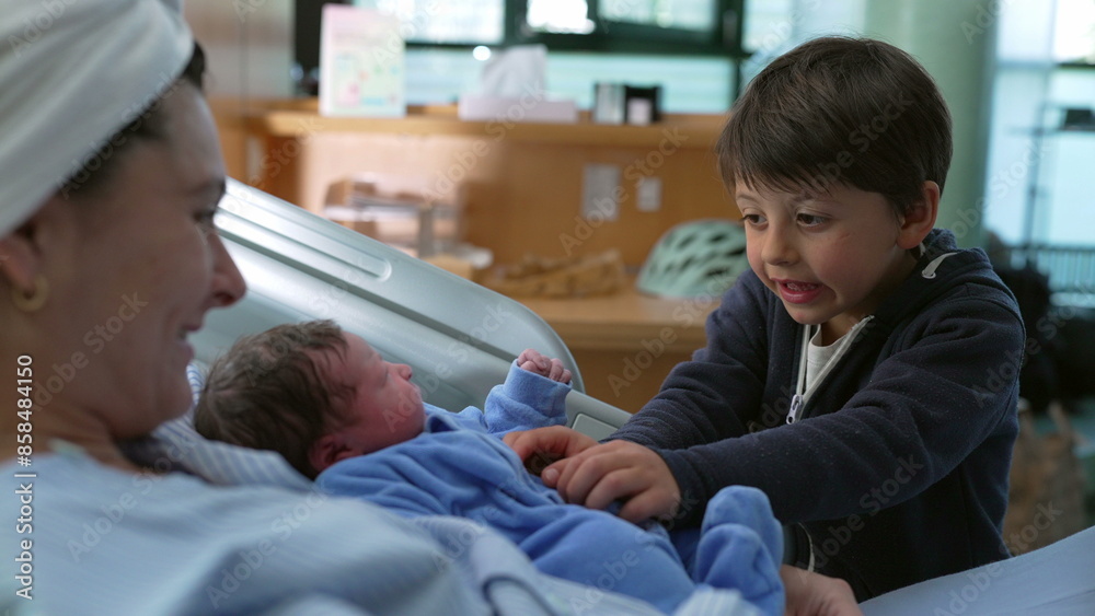 Bonding family moment of sibling interacting with his newborn baby brother at hospital after childbirth while mother watches laid in bed, young boy tickling infant Bonding family moment of sibling interacting with his newborn baby brother at hospital after childbirth while mother watches laid in bed, young boy tickling infant