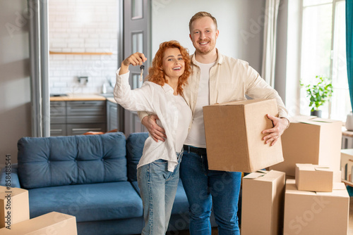 Happy European couple showing keys and man holding cardboard box, moving in new apartment. Insurance, real estate, mortgage concept © Home-stock