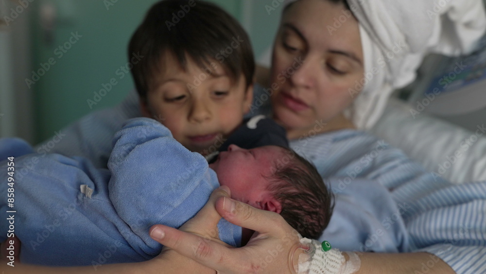 Mother and child welcoming newborn baby in arms at hospital after childbirth. nurse handing little infant to brother's arm next to mom at clinic, siblings bonding for the first time Mother and child welcoming newborn baby in arms at hospital after childbirth. nurse handing little infant to brother's arm next to mom at clinic, siblings bonding for the first time