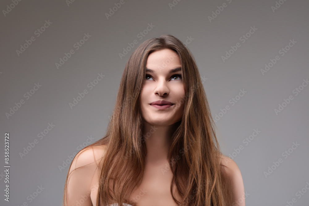 Naklejka premium Beautiful woman looking up with thoughtful expression on grey ba