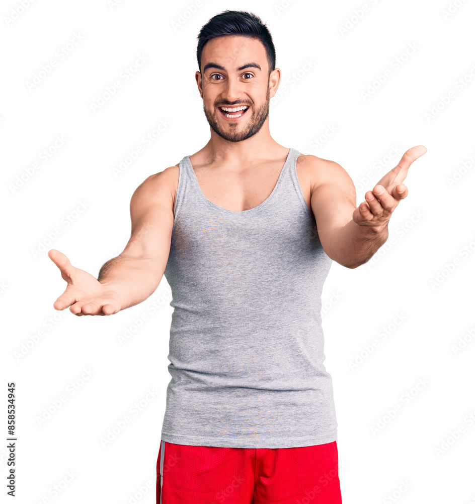 Fototapeta premium Young handsome man wearing swimwear and sleeveless t-shirt smiling cheerful offering hands giving assistance and acceptance.