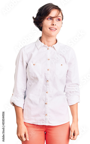Beautiful young woman with short hair wearing elegant white shirt looking away to side with smile on face, natural expression. laughing confident.