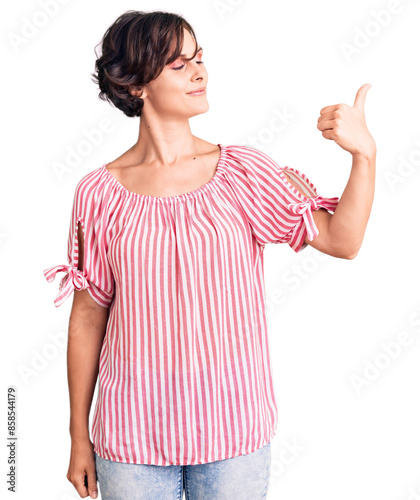 Beautiful young woman with short hair wearing casual summer clothes looking proud, smiling doing thumbs up gesture to the side