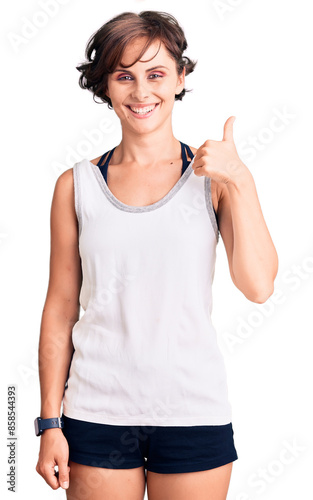 Beautiful young woman with short hair wearing casual sport clothes smiling happy and positive, thumb up doing excellent and approval sign