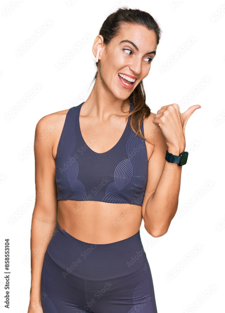 Young beautiful woman wearing sportswear smiling with happy face looking and pointing to the side with thumb up. Young beautiful woman wearing sportswear smiling with happy face looking and pointing to the side with thumb up.
