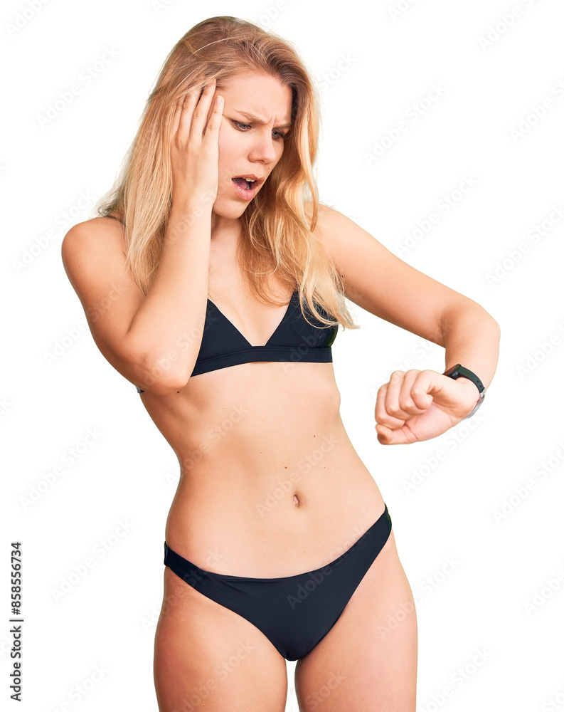 Naklejka premium Young beautiful blonde woman wearing bikini looking at the watch time worried, afraid of getting late