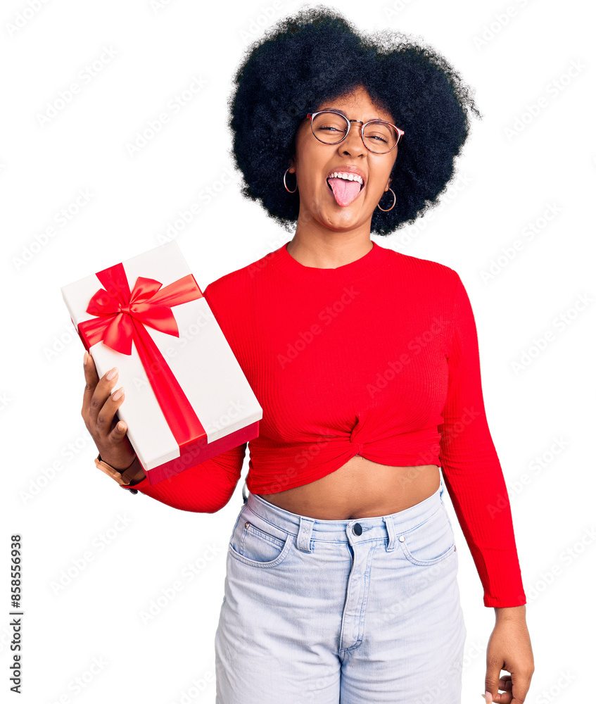 Young african american girl holding gift sticking tongue out happy with funny expression. emotion concept. Young african american girl holding gift sticking tongue out happy with funny expression. emotion concept.