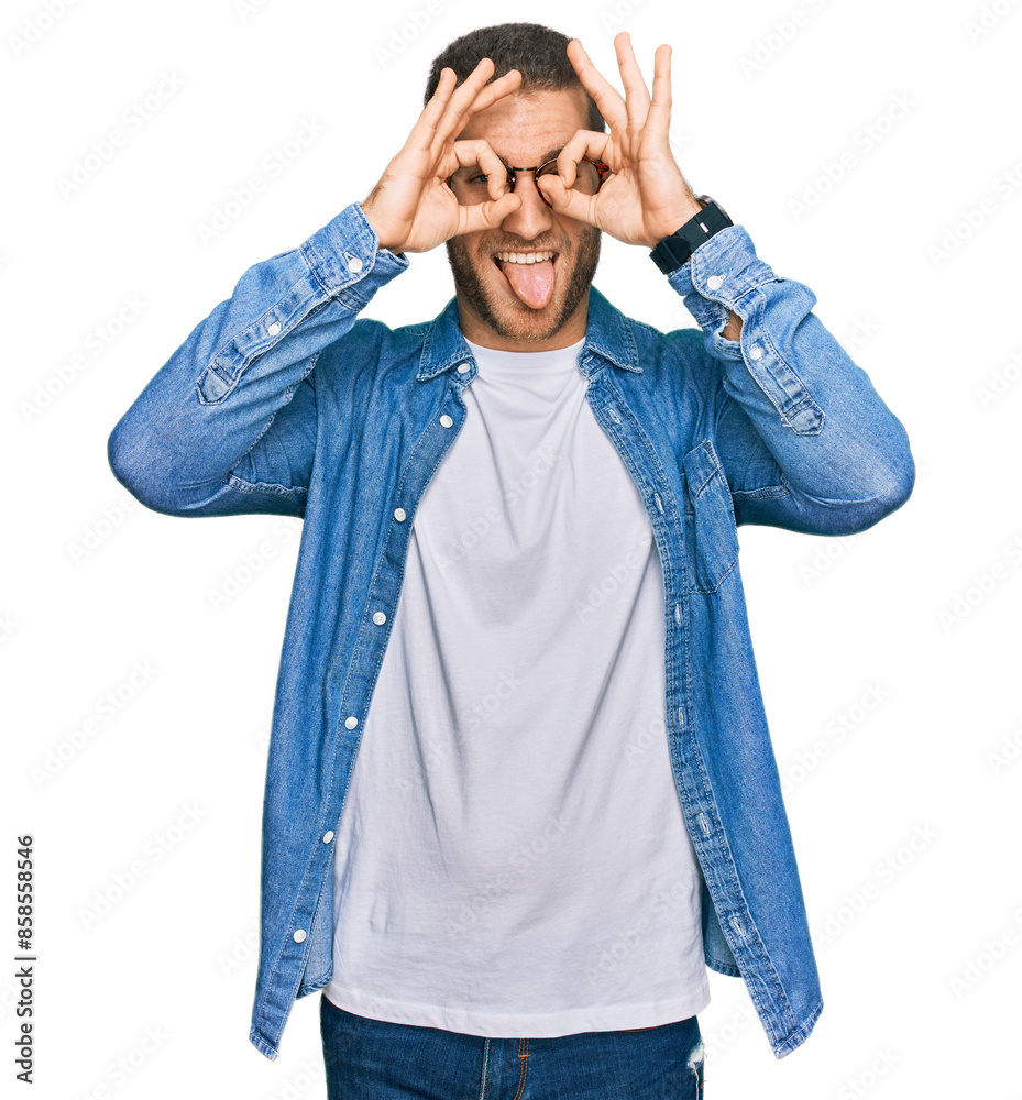 Young caucasian man wearing casual clothes doing ok gesture like binoculars sticking tongue out, eyes looking through fingers. crazy expression. Young caucasian man wearing casual clothes doing ok gesture like binoculars sticking tongue out, eyes looking through fingers. crazy expression.