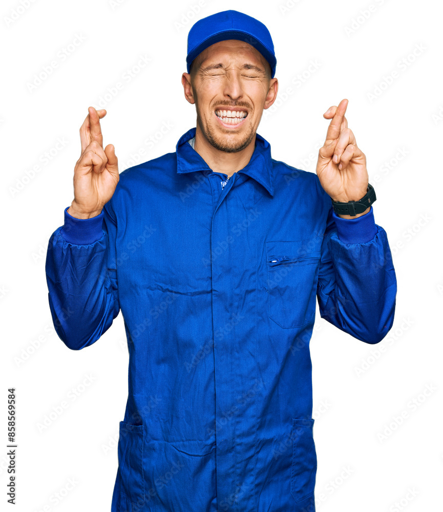 Bald man with beard wearing builder jumpsuit uniform gesturing finger crossed smiling with hope and eyes closed. luck and superstitious concept. Bald man with beard wearing builder jumpsuit uniform gesturing finger crossed smiling with hope and eyes closed. luck and superstitious concept.