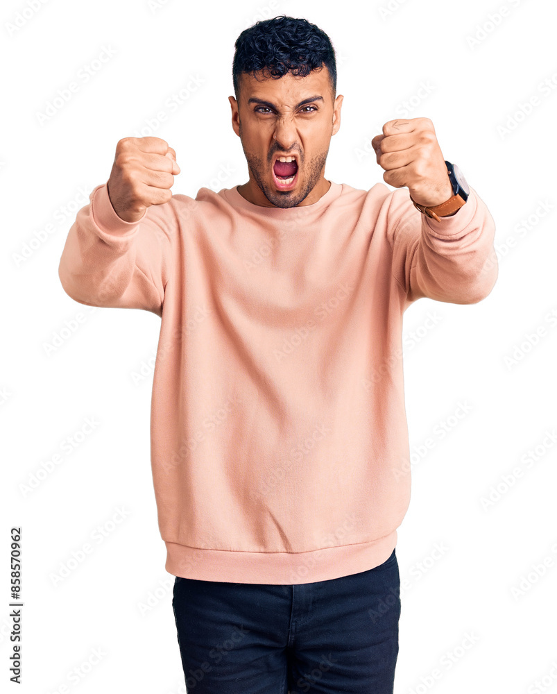 Young hispanic man wearing casual clothes angry and mad raising fists frustrated and furious while shouting with anger. rage and aggressive concept. Young hispanic man wearing casual clothes angry and mad raising fists frustrated and furious while shouting with anger. rage and aggressive concept.