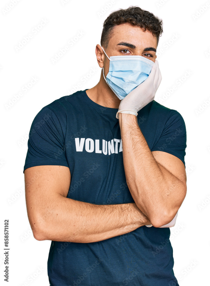 Hispanic young man wearing medical mask and volunteer t shirt thinking looking tired and bored with depression problems with crossed arms. Hispanic young man wearing medical mask and volunteer t shirt thinking looking tired and bored with depression problems with crossed arms.