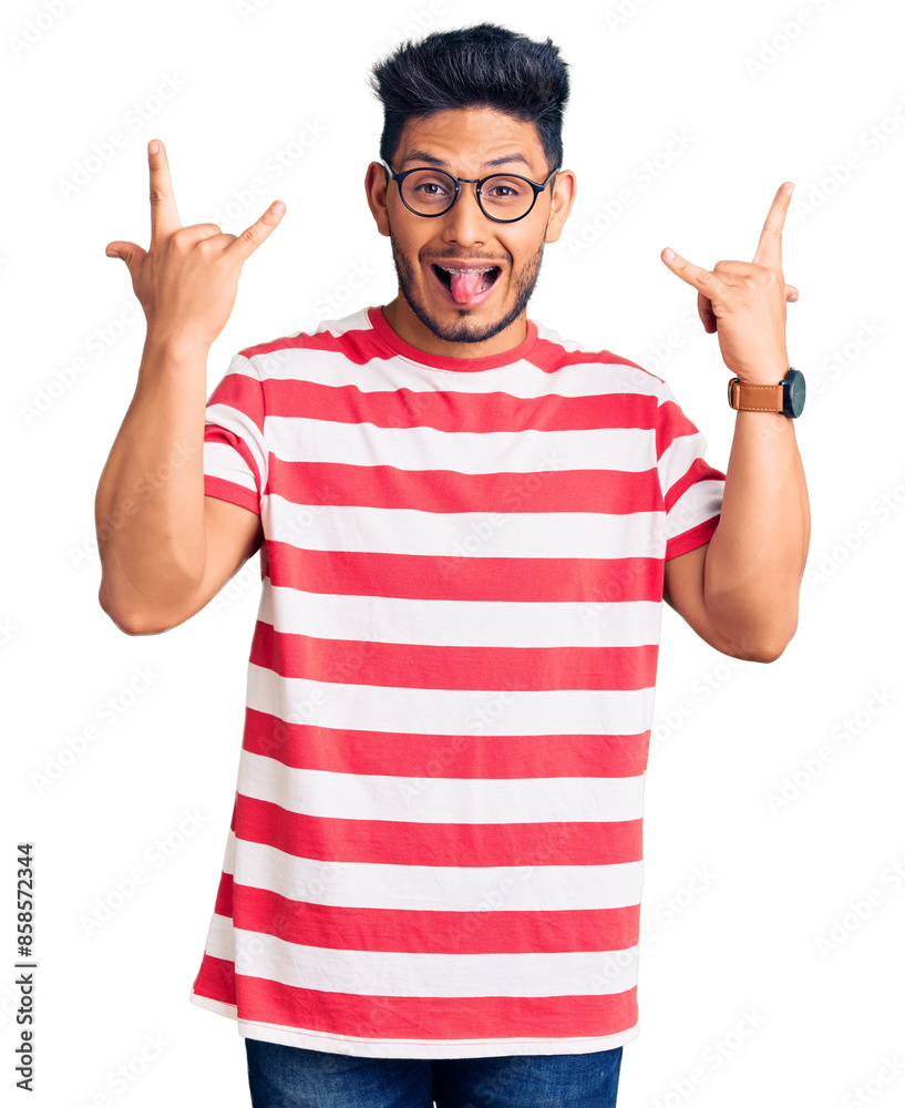 Handsome latin american young man wearing casual clothes and glasses shouting with crazy expression doing rock symbol with hands up. music star. heavy music concept. Handsome latin american young man wearing casual clothes and glasses shouting with crazy expression doing rock symbol with hands up. music star. heavy music concept.
