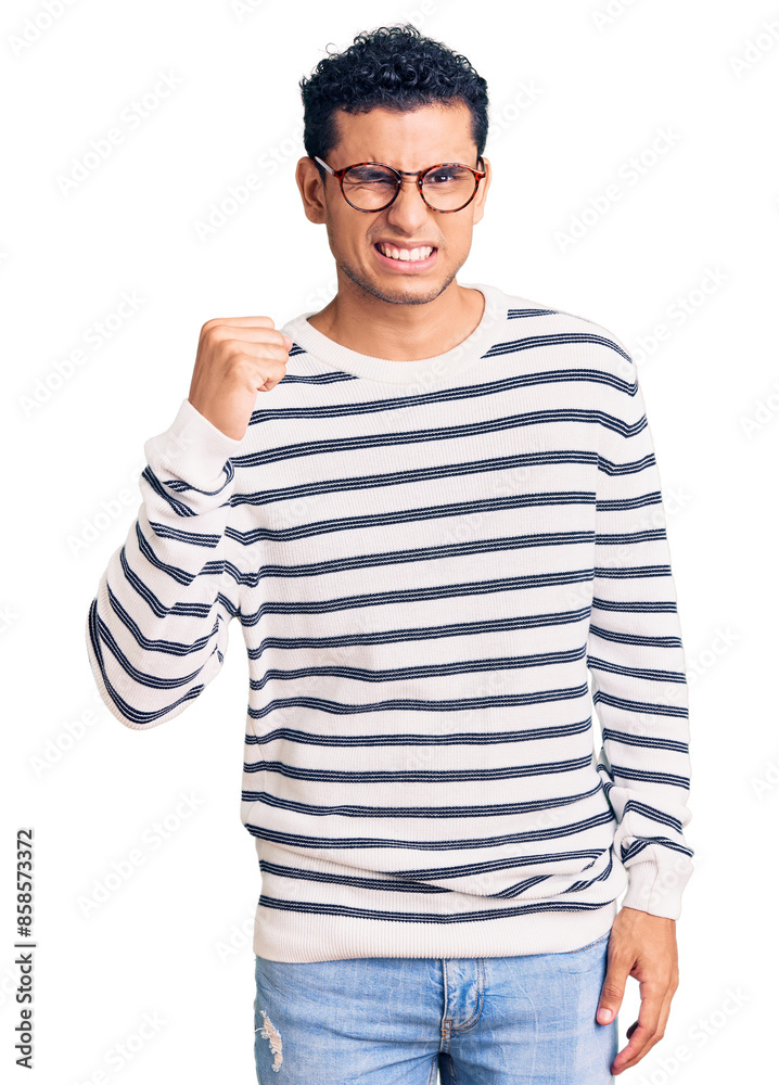 Hispanic handsome young man wearing casual clothes and glasses angry and mad raising fist frustrated and furious while shouting with anger. rage and aggressive concept.