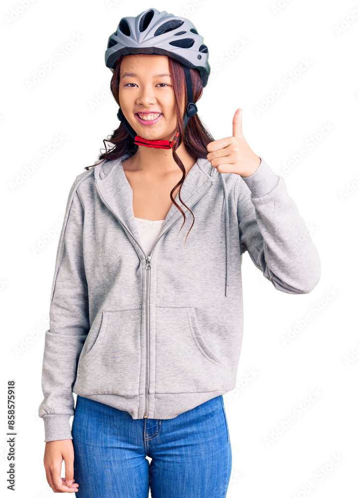 Young beautiful chinese girl wearing bike helmet smiling happy and positive, thumb up doing excellent and approval sign Young beautiful chinese girl wearing bike helmet smiling happy and positive, thumb up doing excellent and approval sign