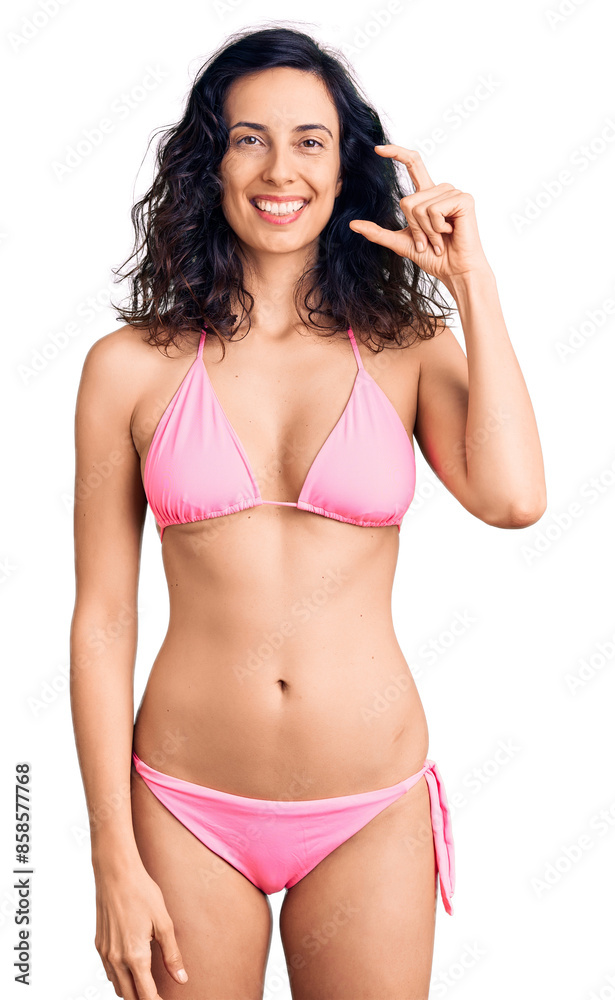 Naklejka premium Young beautiful hispanic woman wearing bikini smiling and confident gesturing with hand doing small size sign with fingers looking and the camera. measure concept.