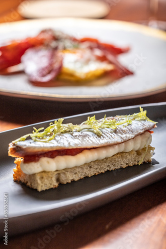 Obraz w ramie Chef prepara una tostada con anchoa y sardina ahumada con crema de queso, mermelada de tomate y escarola en un restaurante 