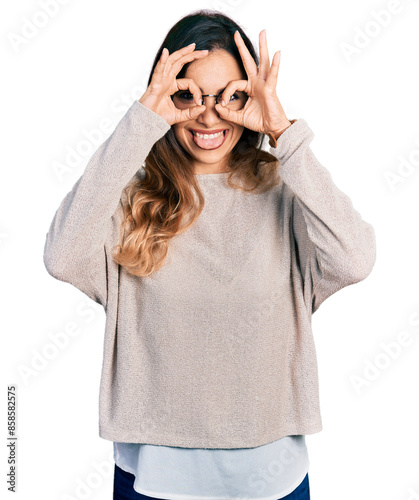 Beautiful hispanic woman wearing casual sweater and glasses doing ok gesture like binoculars sticking tongue out, eyes looking through fingers. crazy expression. © Krakenimages.com