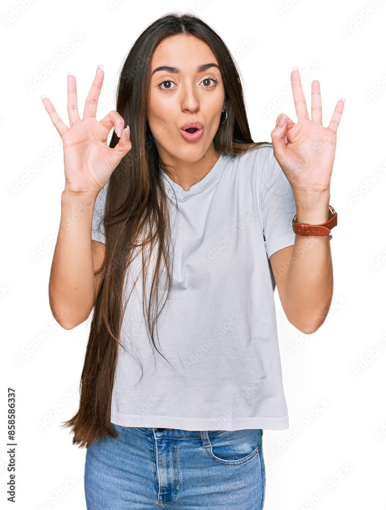 Young hispanic girl wearing casual white t shirt looking surprised and shocked doing ok approval symbol with fingers. crazy expression Young hispanic girl wearing casual white t shirt looking surprised and shocked doing ok approval symbol with fingers. crazy expression