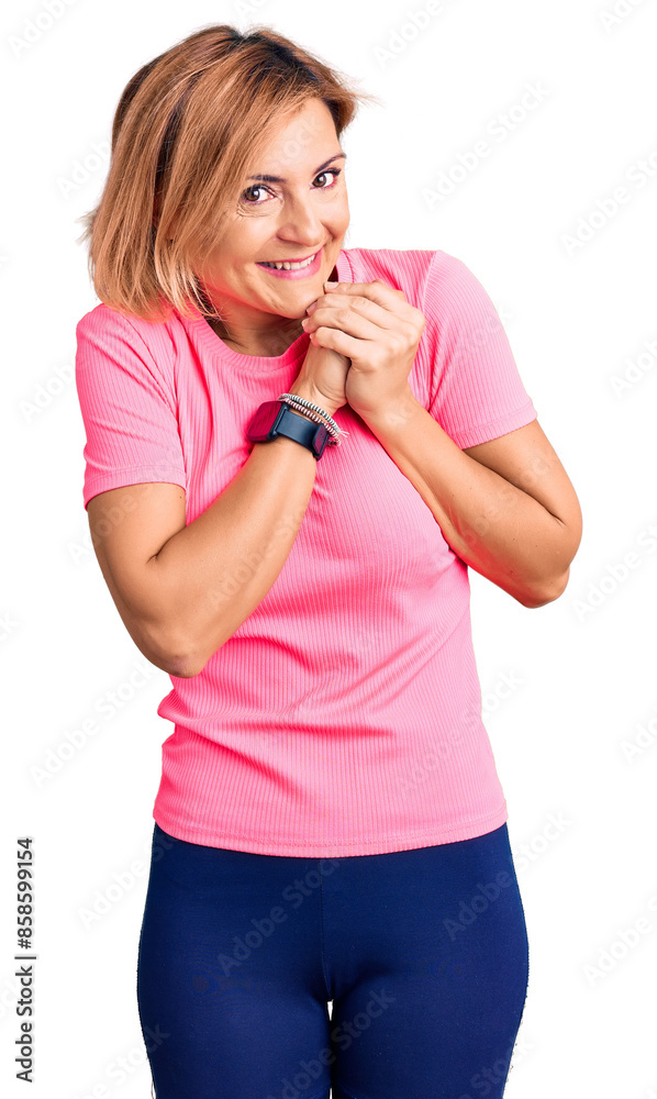 Young blonde woman wearing sportswear laughing nervous and excited with hands on chin looking to the side Young blonde woman wearing sportswear laughing nervous and excited with hands on chin looking to the side