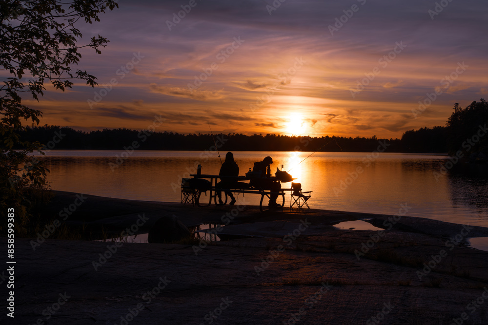 A group of people are sitting on a bench by a lake, watching the sun set A group of people are sitting on a bench by a lake, watching the sun set