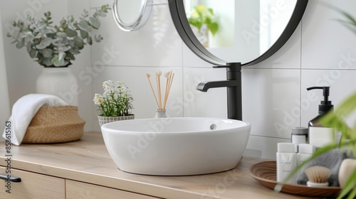 Stylish Bathroom Decor - White sink with black fixtures, light wood cabinet, a round mirror, and minimalist accessories