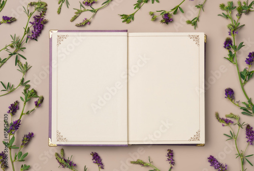 Open empty notebook in vintage style with frame of flowers on beige background from above. Flat lay, top view. Copy space