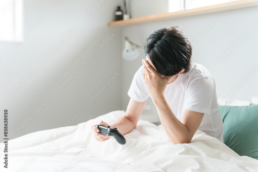 家のベッドルーム・寝室でゲームをする男性ゲーマー（負ける・悔しい・課金）
