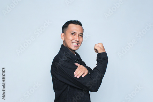 Asian man wearing jacket showing strong gesture by lifting her arms and muscles smiling proudly on the white background. photo