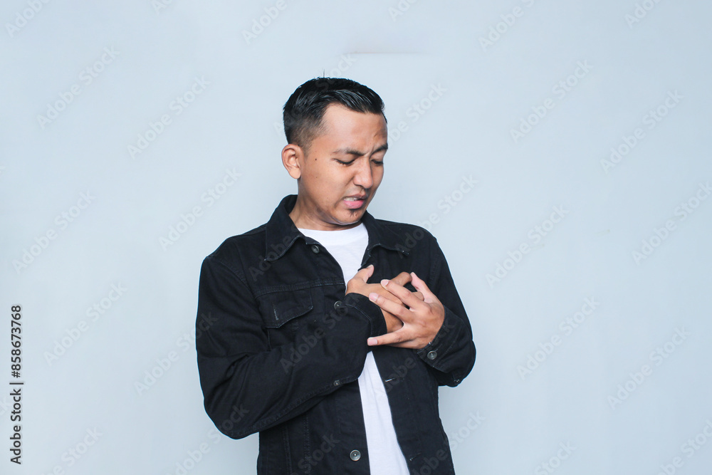 Asian young man wearing black jacket holding his chest. Healthcare concept. Asian young man wearing black jacket holding his chest. Healthcare concept.