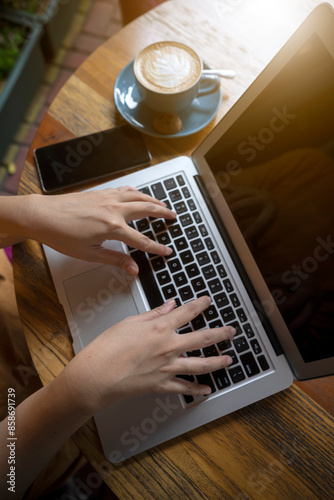 A person is typing on a laptop while holding a cup of coffee