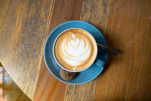 A blue coffee cup with a white leaf design on it sits on a wooden table