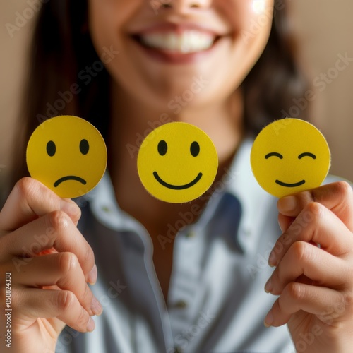 Three yellow emoticons expressing different emotions held by a smiling person