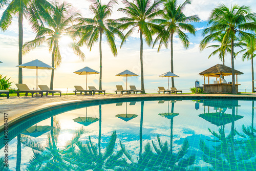 Beautiful luxury umbrella and chair around outdoor swimming pool in hotel and resort with coconut palm tree on sunset or sunrise sky