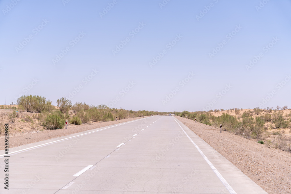A road with no cars on it. The sky is clear and blue. The road is empty and straight