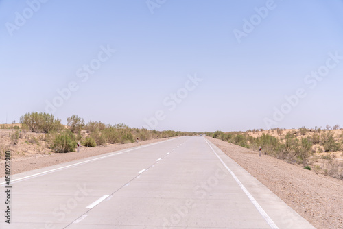 A road with no cars on it. The sky is clear and blue. The road is empty and straight