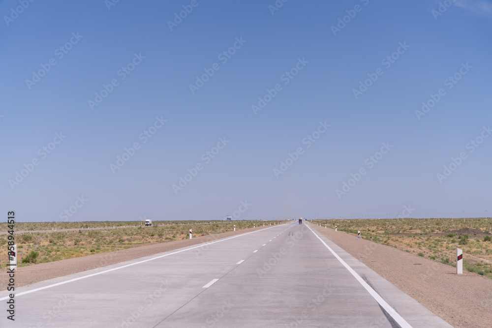 A long, empty road with no cars or people. The sky is clear and blue. The road is made of concrete and has white lines painted on it A long, empty road with no cars or people. The sky is clear and blue. The road is made of concrete and has white lines painted on it