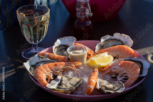 Seafood tasting plate as promo on the oysters' farm in the South of France. Traditional Mediterranean seaside lunch or dinner - white wine, shrimp, oysters, aioli sauce, lemon, and vinegar.