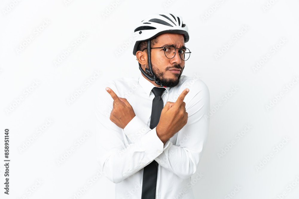 Young business latin man holding a bike helmet isolated on white background pointing to the laterals having doubts Young business latin man holding a bike helmet isolated on white background pointing to the laterals having doubts