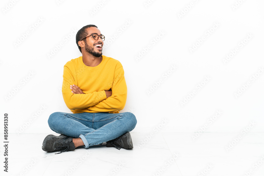 Young Ecuadorian man sitting on the floor isolated on white wall happy and smiling Young Ecuadorian man sitting on the floor isolated on white wall happy and smiling