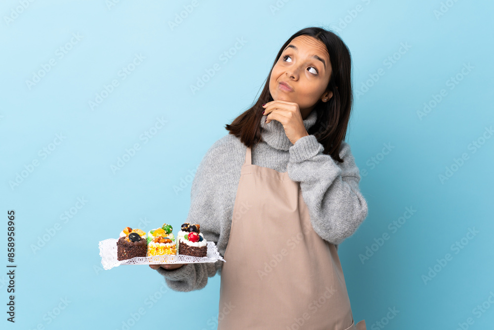 Pastry chef holding a big cake over isolated blue background and looking up. Pastry chef holding a big cake over isolated blue background and looking up.