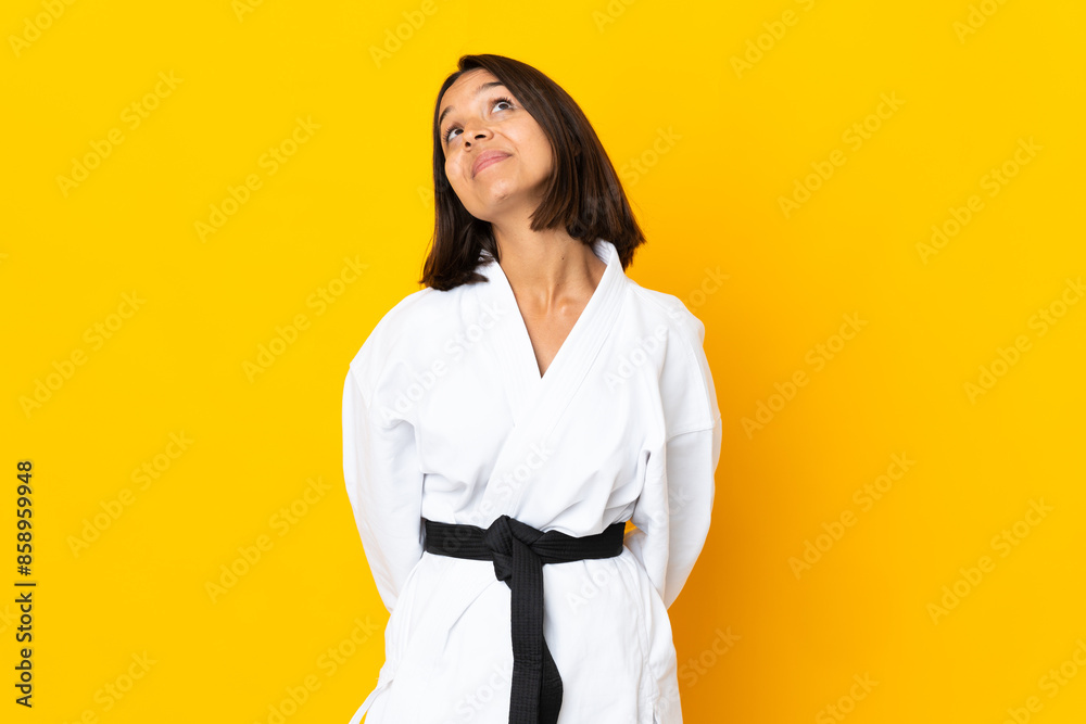 Young woman doing karate isolated on yellow background and looking up Young woman doing karate isolated on yellow background and looking up