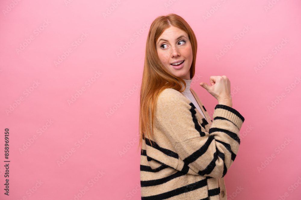 Young redhead woman isolated on pink background pointing to the side to present a product Young redhead woman isolated on pink background pointing to the side to present a product