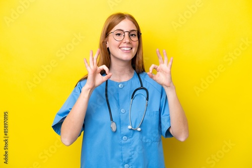 Young redhead nurse woman isolated on yellow background showing an ok sign with fingers